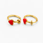 A pair of gold huggie hoop earrings, each adorned with a small red heart charm, displayed on a clean white background.
