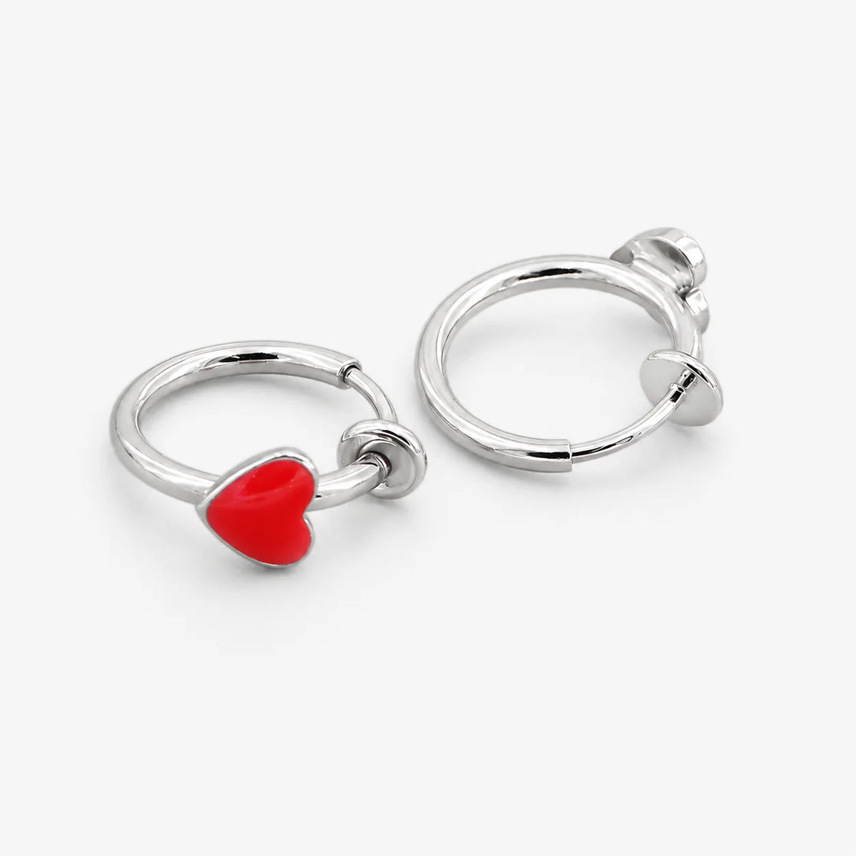 A pair of silver-toned hoop earrings, each featuring a small, polished red heart charm, displayed on a clean white background.
