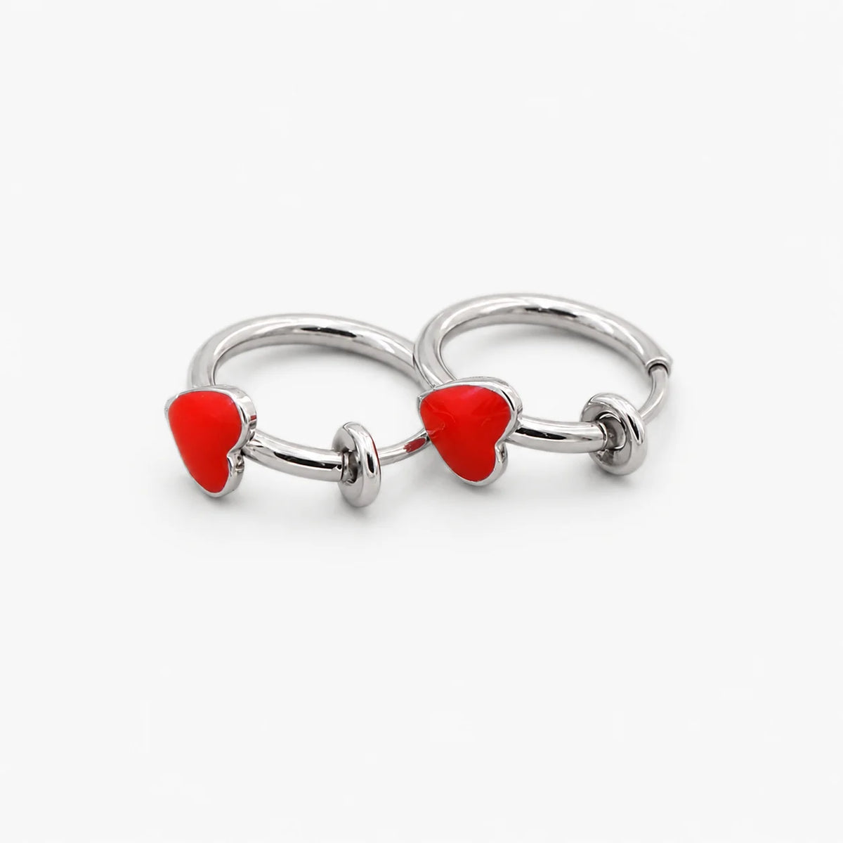 Two silver-toned hoop earrings, each featuring a small red heart charm, displayed on a clean white background.