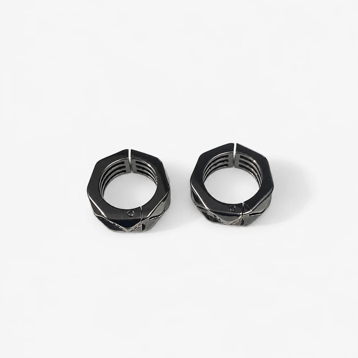 A close-up, top-down view of a black athletic clip on earrings with textured tread patterns, set against a solid light gray background.