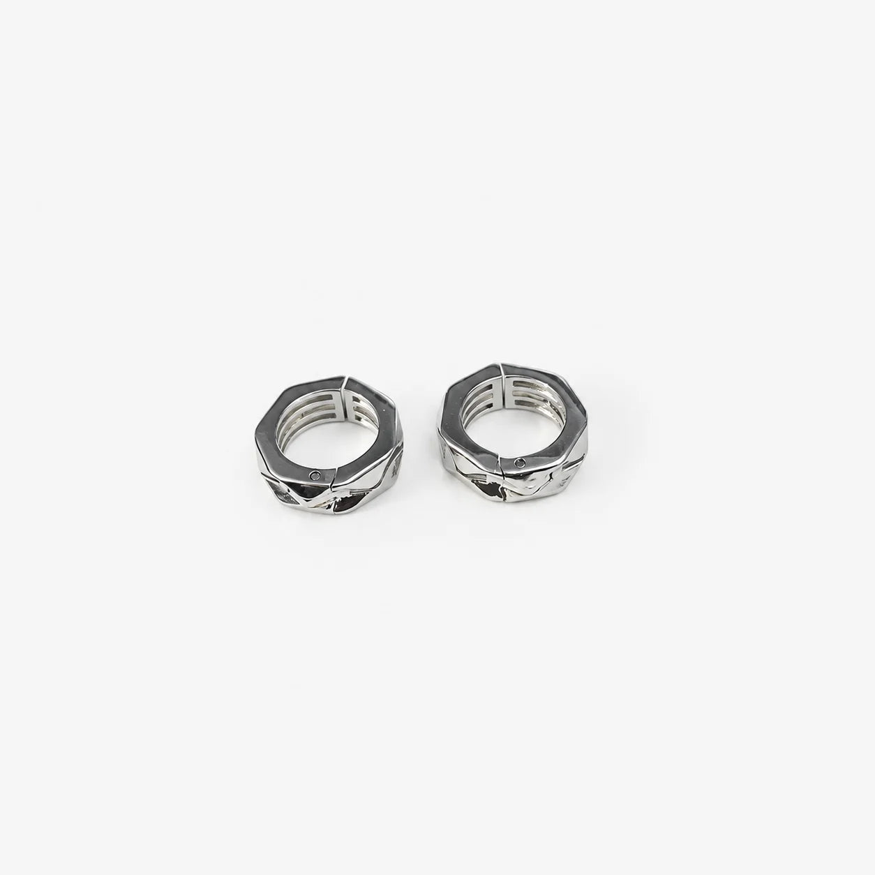 A close-up, top-down view of a silver athletic clip on earrings with textured tread patterns, set against a solid light gray background.