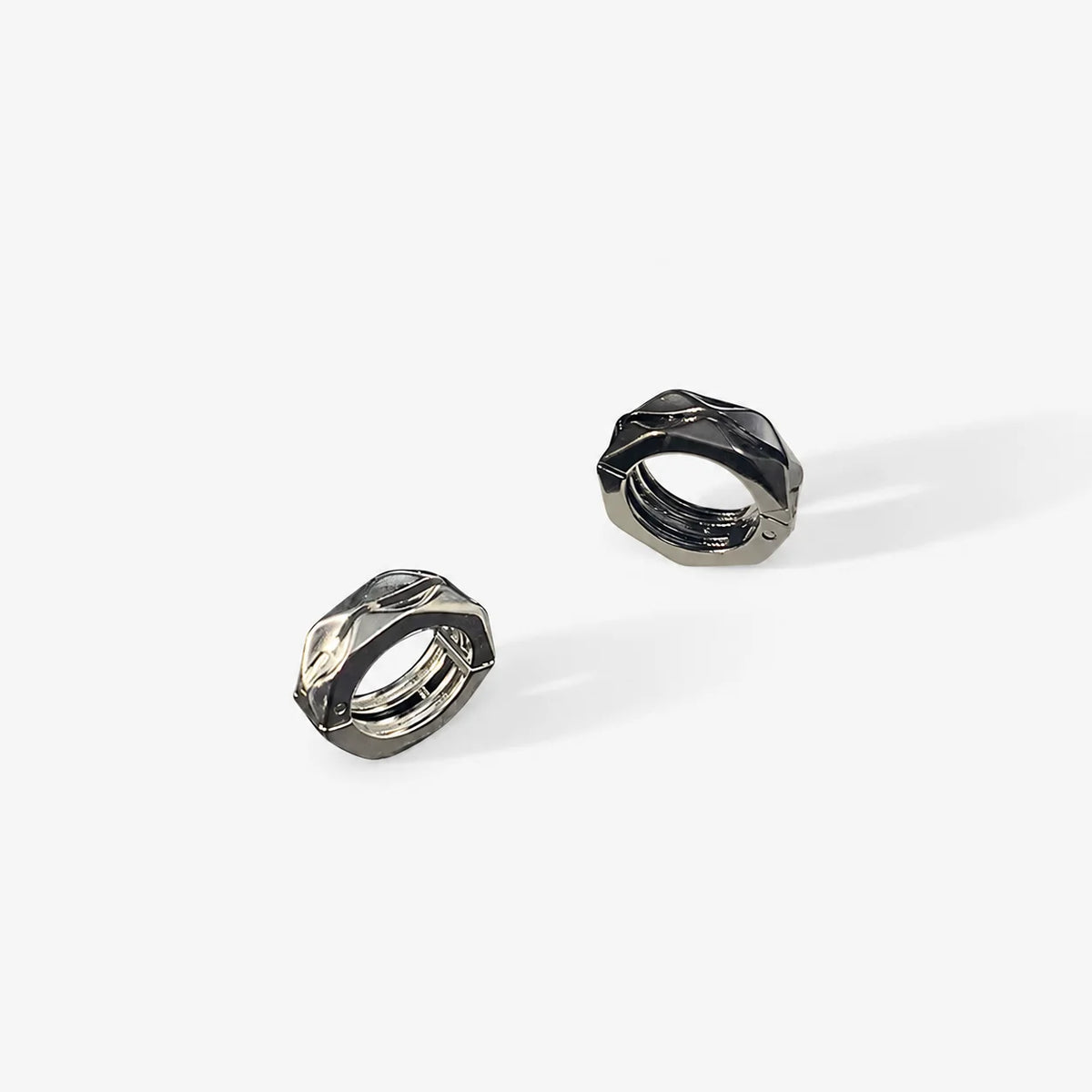 A pair of faceted metallic clip on hoop earrings in a dark gunmetal gray finish, displayed on a clean white background.