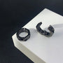 Black hex cut clip-on hoop earrings displayed on white stand, angled front view against dark background