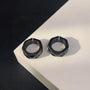 Black hex cut clip-on hoop earrings displayed on white surface against dark background