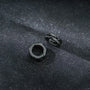 Black hex cut clip-on hoop earrings displayed on dark sparkly surface, showing geometric design and metallic finish from above
