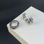 Silver hex cut clip-on hoop earrings displayed on white stand, angled side view against dark background