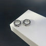 Hex cut clip-on hoop earrings in silver displayed on white platform against dark background