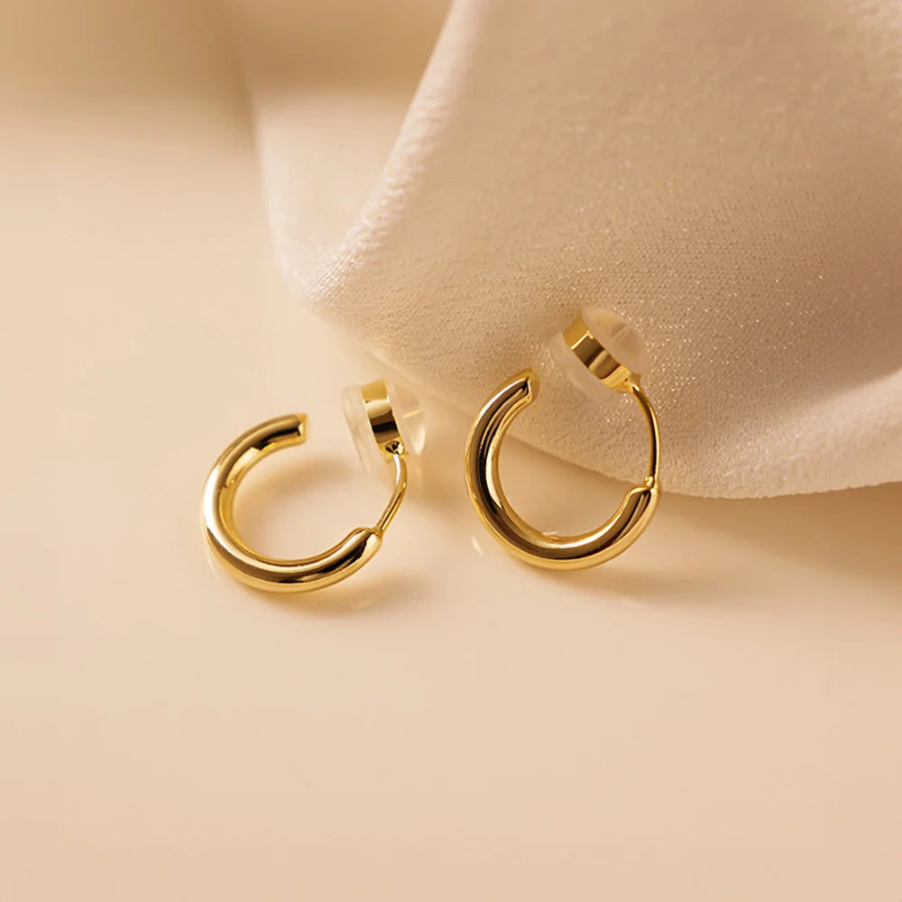 A pair of gold huggie clip on hoop earrings displayed in a lifestyle photo.