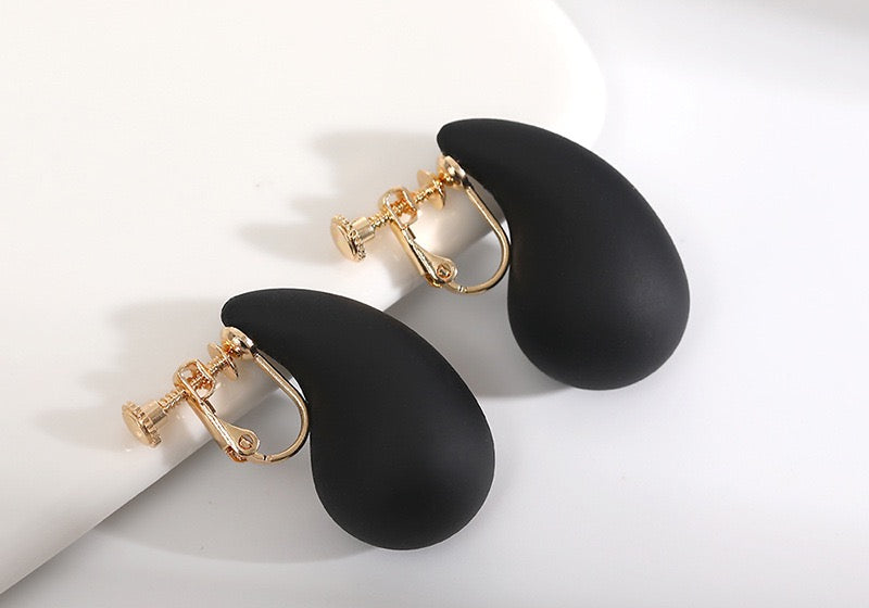  Modern black teardrop clip-on earrings with a matte finish. These chunky, tear-shaped earrings are made from a durable alloy with a screw-back clip-on design, providing a comfortable and secure fit for anyone without pierced ears. They're a sophisticated addition to any contemporary jewelry collection.