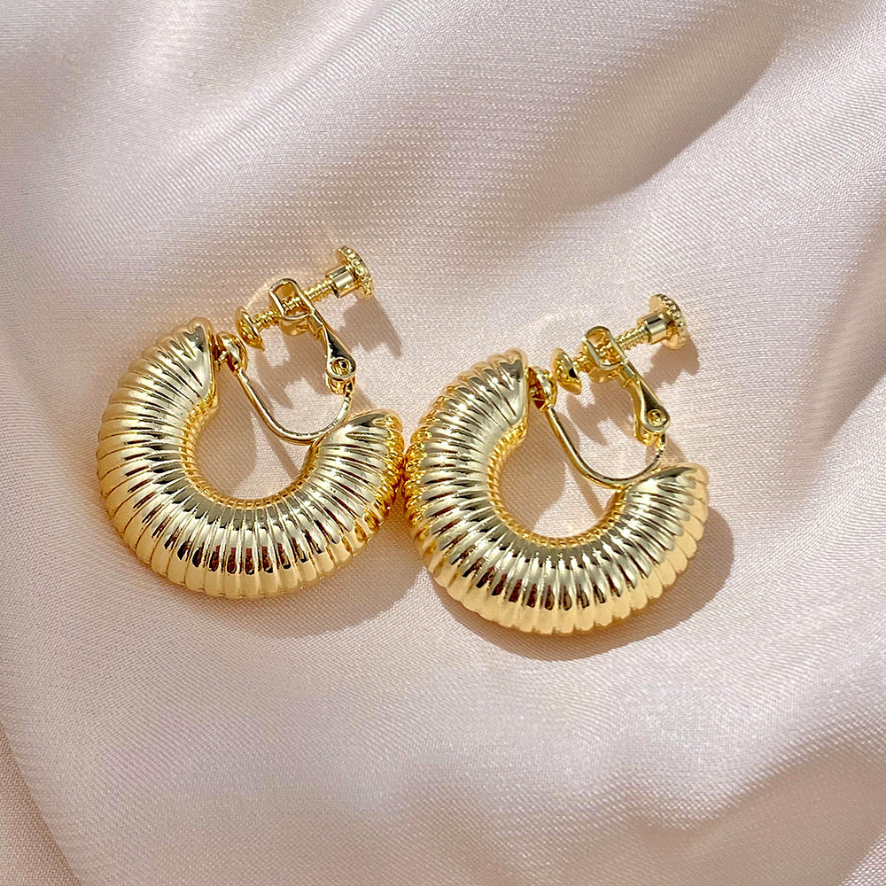 Lustrous gold-tone helix hoop clip-on earrings, designed with a modern twist, made from copper alloy and featuring a screw-back clip-on closure. These huggie-style earrings offer sophistication without the need for piercing.