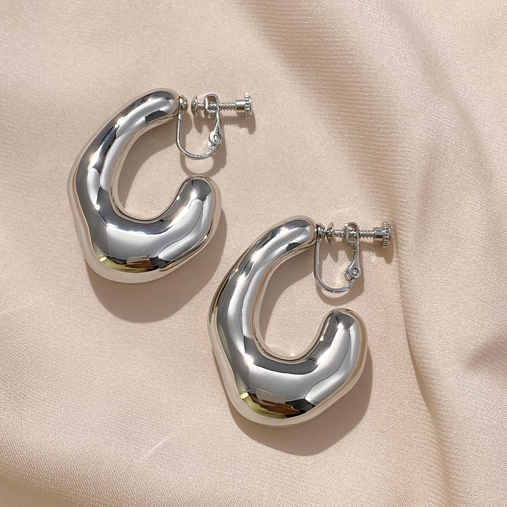 Chunky silver clip-on hoop earrings feature a curved design for a touch of contemporary style. Crafted from alloy with a secure screw-back closure, they're perfect for those who love bold statement jewelry.