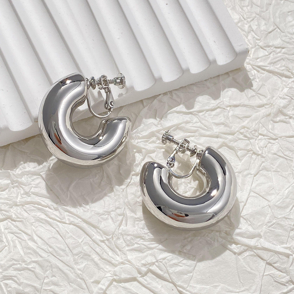 Polished silver-tone bold hoop clip-on earrings with a modern flair, constructed from a copper alloy. These huggie-style earrings feature a secure screw-back clip-on closure, perfect for a contemporary look.