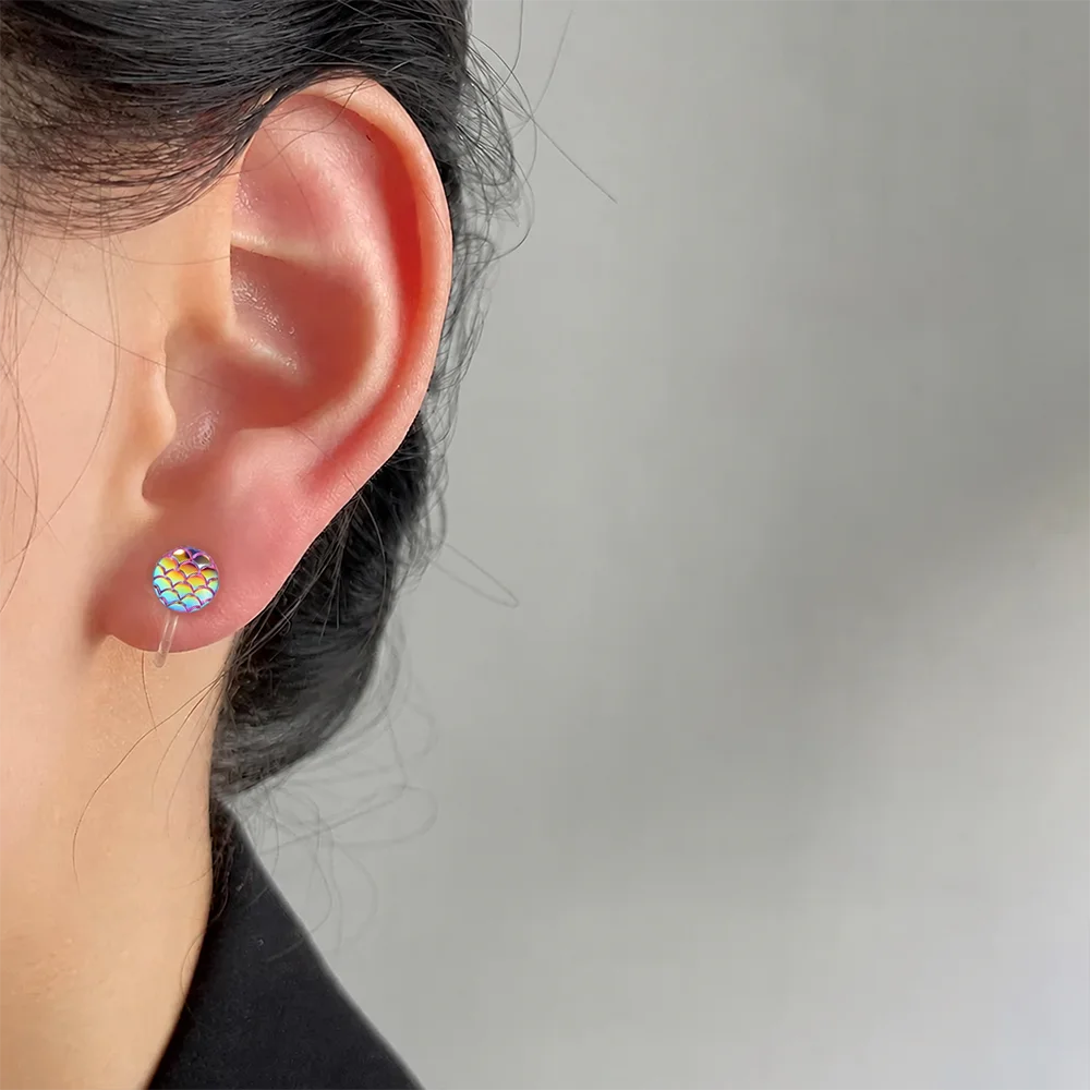 A close-up of a person's ear wearing a small round stud earring with a colorful, patterned design on a plain light gray background.