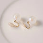Iridescent pearl clip-on earrings with gold hooks displayed on white surface, overhead view