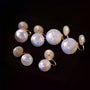 A set of iridescent white pearl stud earrings with gold-toned spiral and hook settings, displayed on a solid black background.