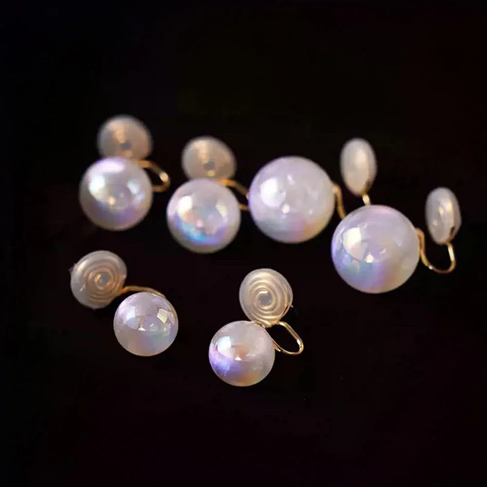 A set of iridescent white pearl stud earrings with gold-toned spiral and hook settings, displayed on a solid black background.