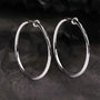 Large silver hoop clip-on earrings displayed at an angle on dark textured surface showing polished finish and closure detail