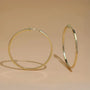 Gold large square tube clip-on hoop earrings displayed at angles on neutral beige background