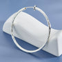 Large twisted textured silver hoop clip-on earrings displayed on white ceramic stand against blue background