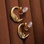 Lunar Face Gold Rotating Clip-On Earrings displayed on brown fabric, showing detailed moon face design and transparent backing clips
