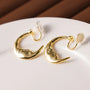 Gold Lunar Face rotating clip-on earrings displayed on white surface, front angle view showing polished finish and cream backing details