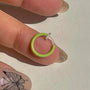 Mini glow clip-on hoop earrings in bright green held in hand on white background