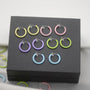 Mini glow clip-on hoop earrings in yellow, pink, purple and blue displayed on black presentation box