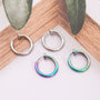 Mini hoop clip on earrings in silver and rainbow colors displayed on wooden surface with greenery detail