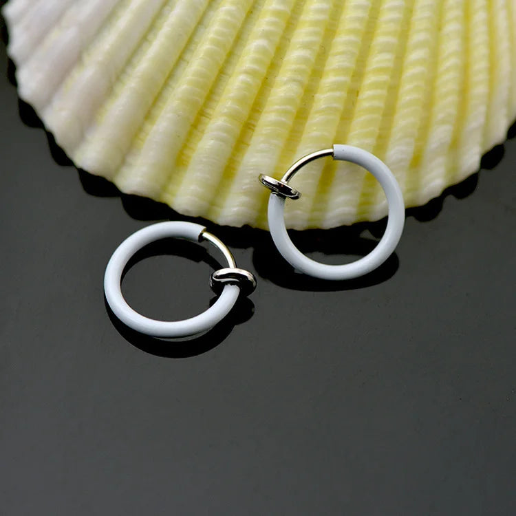White mini hoop clip-on earrings displayed at an angle with a shell backdrop on gray surface