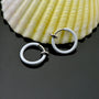 White mini hoop clip-on earrings displayed at an angle with a shell backdrop on gray surface
