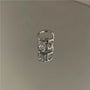 Minimalist white zirconia band ear cuff top view on neutral background showcasing silver metal design