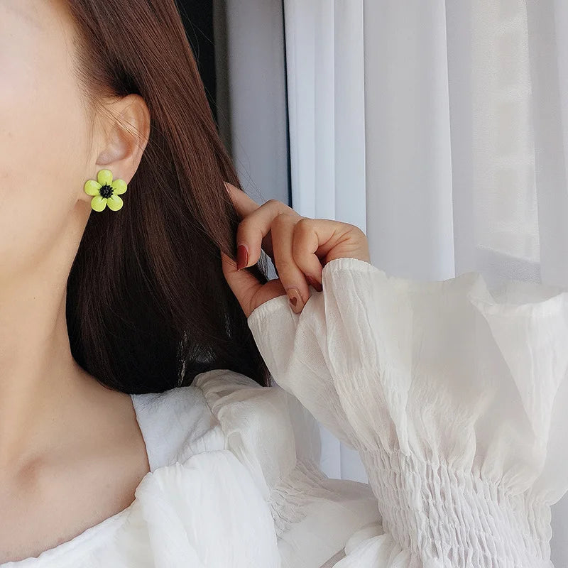 Lime Blossom Clip-On Earrings worn on ear, side view, neon yellow flower design with black center detail