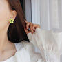 Lime Blossom Clip-On Earrings worn on ear, side view, neon yellow flower design with black center detail