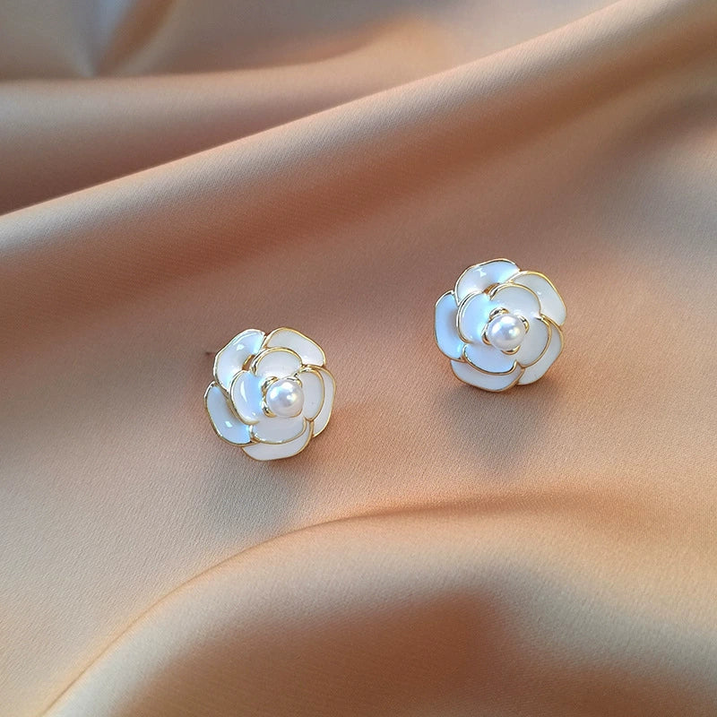 White Camellia enamel clip-on earrings with pearl centers displayed on skin, showing detailed flower design from front angle