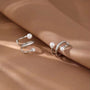 Pearl and Zirconia double-band silver ear cuffs displayed on beige fabric, showcasing elegant curved design with pearl accents and sparkly detail