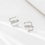 A pair of silver wrap-style hoop earrings with small clear stones and white pearl beads, photographed on a clean white surface.