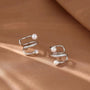 Pearl & Zirconia Double-Band Silver Ear Cuffs displayed on tan fabric, showing front angle view of the elegant spiral design with pearls and crystal accents