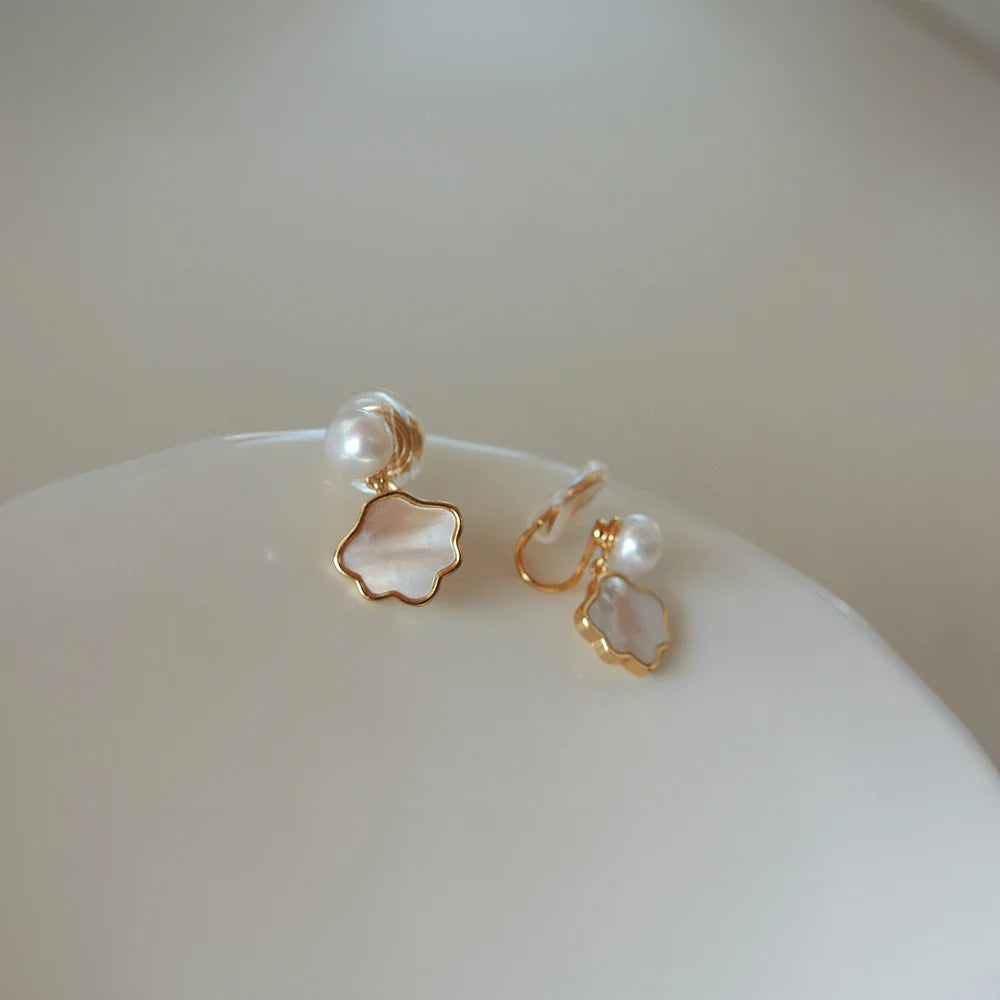 Genuine Pearl and Shell Clip On Earrings in gold with mother of pearl flower charms, top view on white bowl
