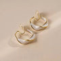 Pearlescent Wave Clip-On Hoop Earrings in gold and white, angled view on beige background