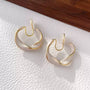 Pearlescent Wave Clip-On Hoop Earrings in gold and iridescent white, front view on textured white background