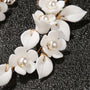 White petal pearl cascade clip-on earrings with gold accents displayed on dark sparkly surface