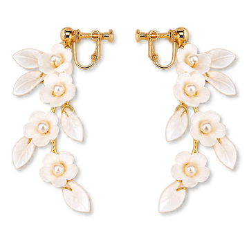 A pair of gold-tone drop earrings featuring white enamel flowers with pearl centers and leaf-shaped enamel details, shown on a plain white background.