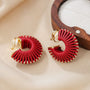 Red leather wrapped clip-on hoop earrings displayed flat on beige fabric with wooden holder detail