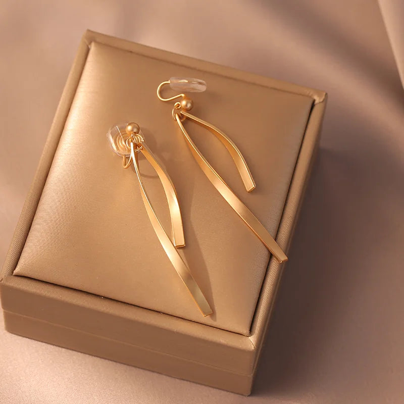 Gold ribbon dangle clip-on earrings in elegant gift box, overhead angle view on beige background