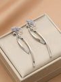 Silver ribbon dangle clip-on earrings displayed on cream jewelry box, overhead view showing sleek metallic design