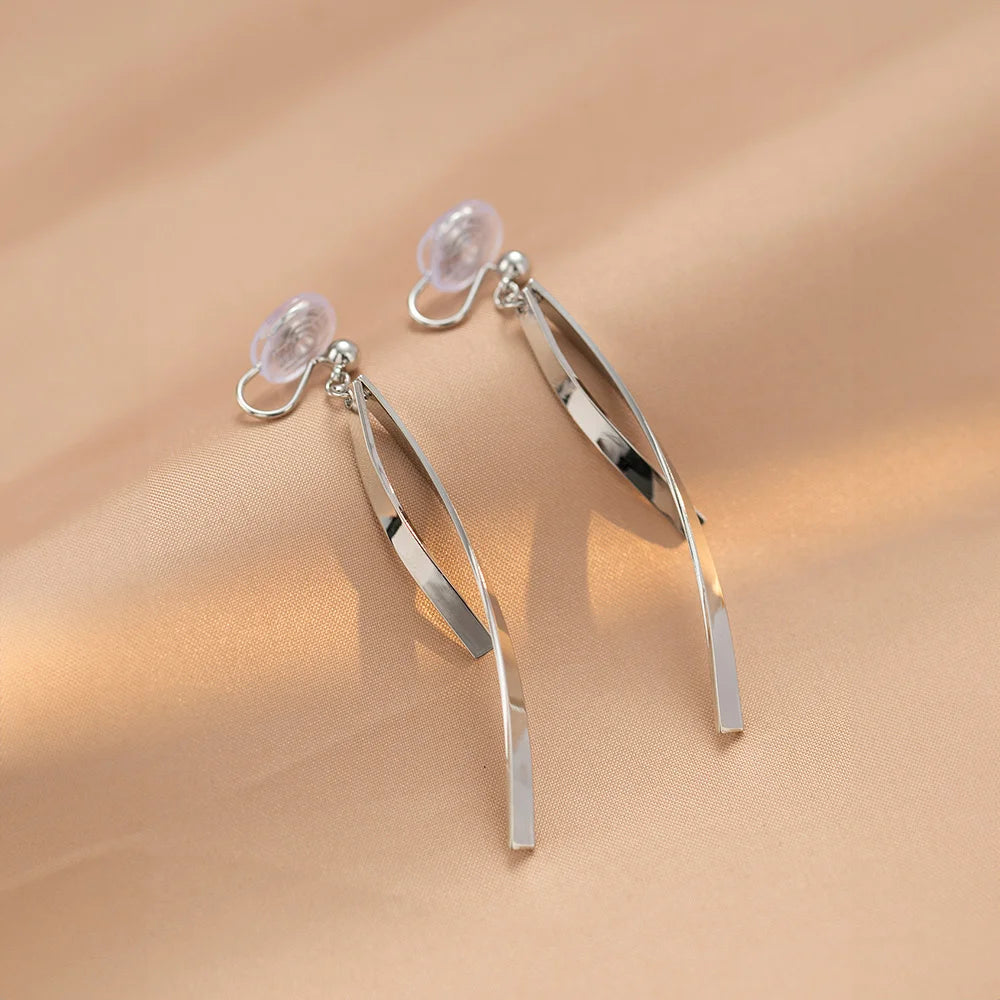 Silver ribbon dangle clip-on earrings front view displayed on beige fabric background