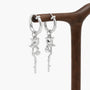 A pair of silver hoop earrings with dangling tree-bud charms, displayed on a dark wooden hanger against a clean white background.