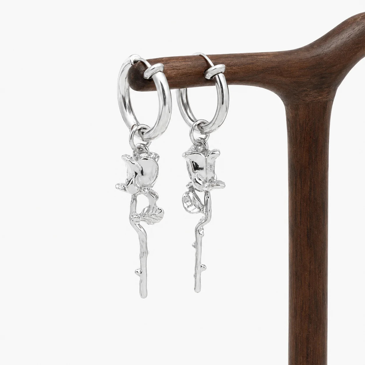 A pair of silver hoop earrings with dangling tree-bud charms, displayed on a dark wooden hanger against a clean white background.