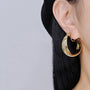 Gold rotating spiral clip-on hoop earrings side view worn on model with black hair against white background
