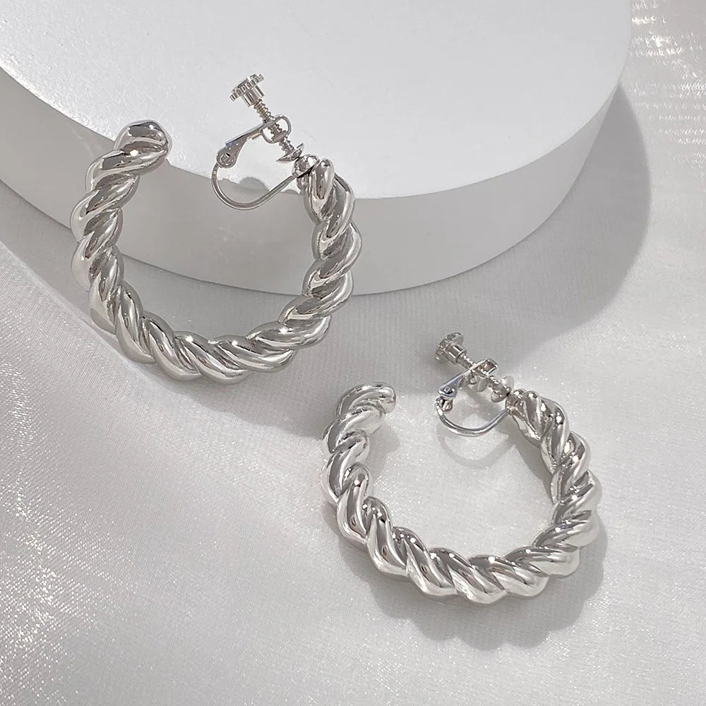 Silver twist hoop clip-on earrings displayed on white surface showing three angle views of the twisted design